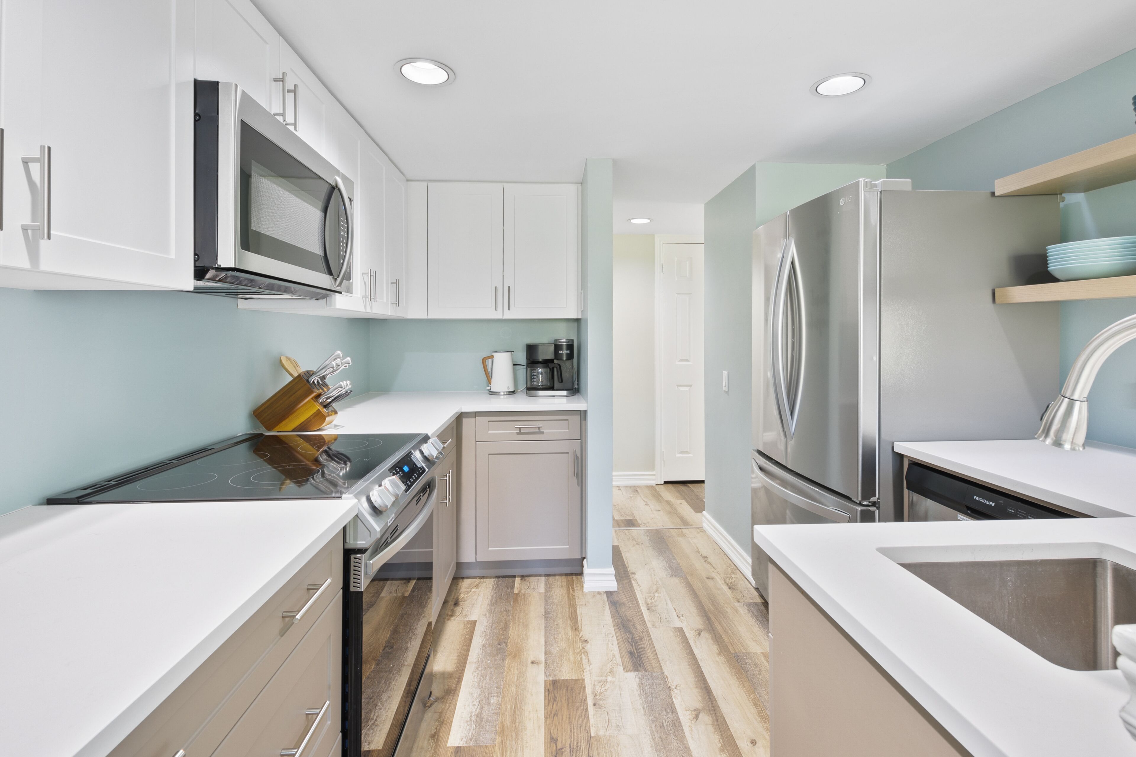 Una cocina moderna con armarios blancos, electrodomésticos de acero inoxidable y piso de madera.