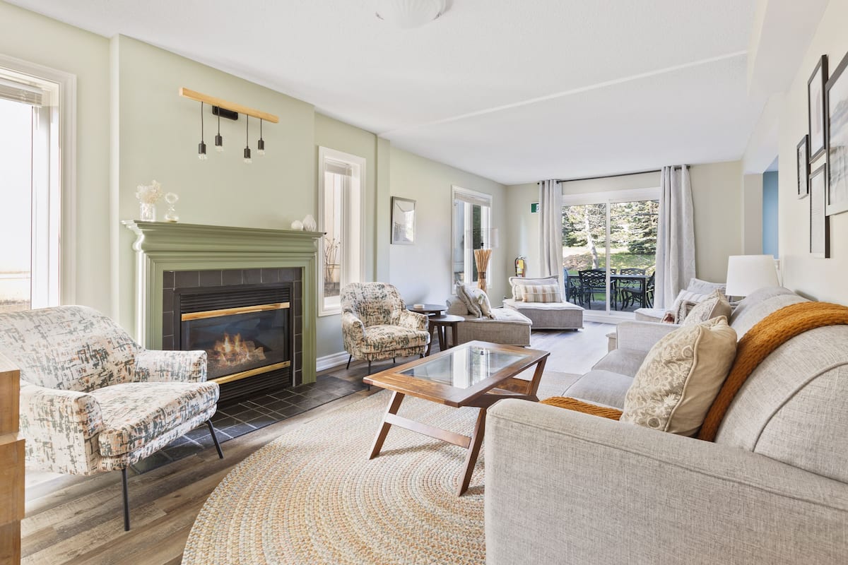 A living room with a fireplace, patterned armchairs, a glass coffee table, and a sofa.