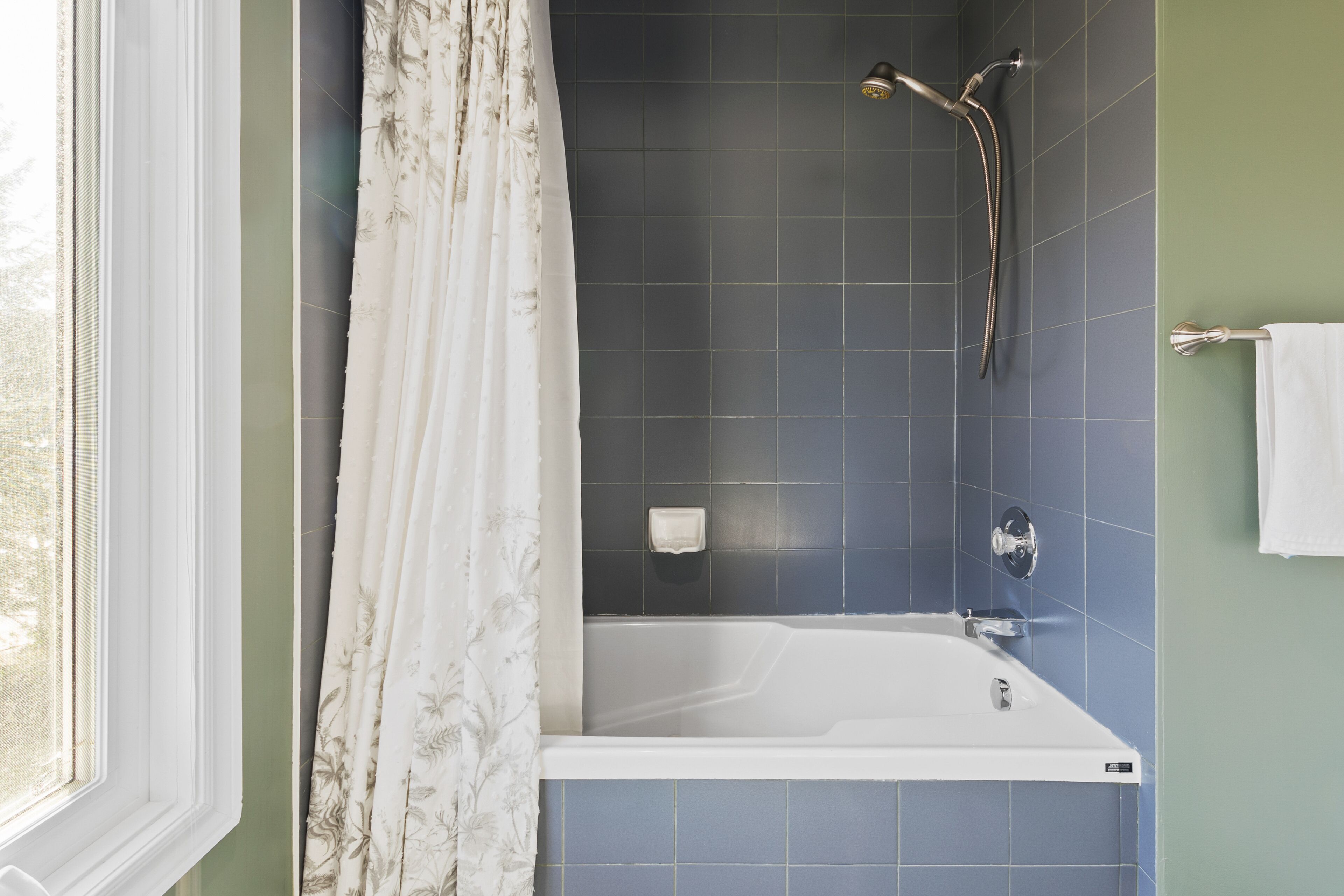 A bathroom with a bathtub, a shower head, and a towel rack.