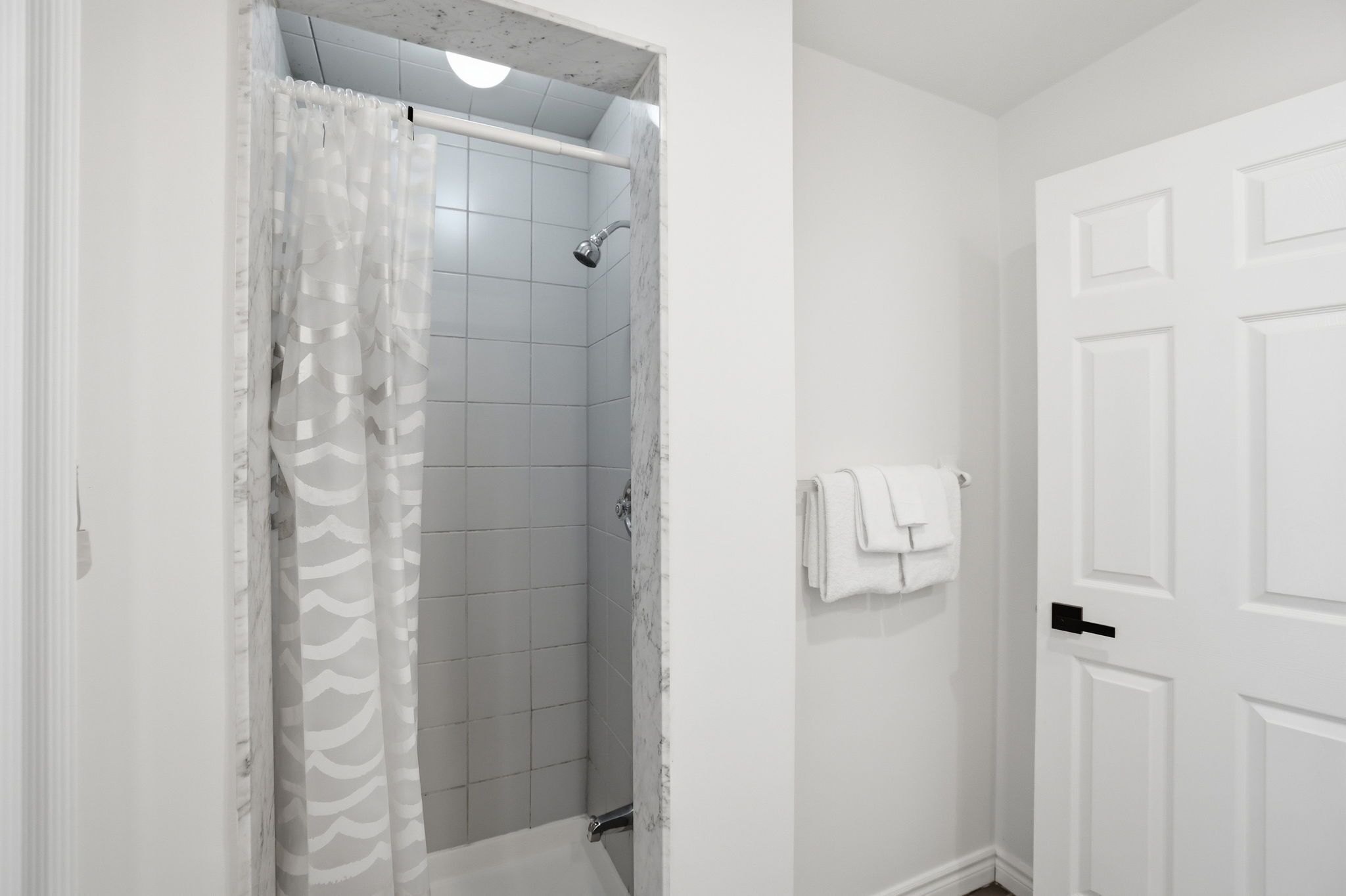 Un baño con ducha, una puerta blanca y un perchero para toallas.
