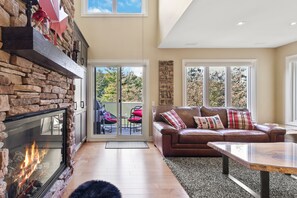 A living room with a stone fireplace, a leather sofa, and a glass coffee table. - Sierra Lane Condos (The Blue Mountains)