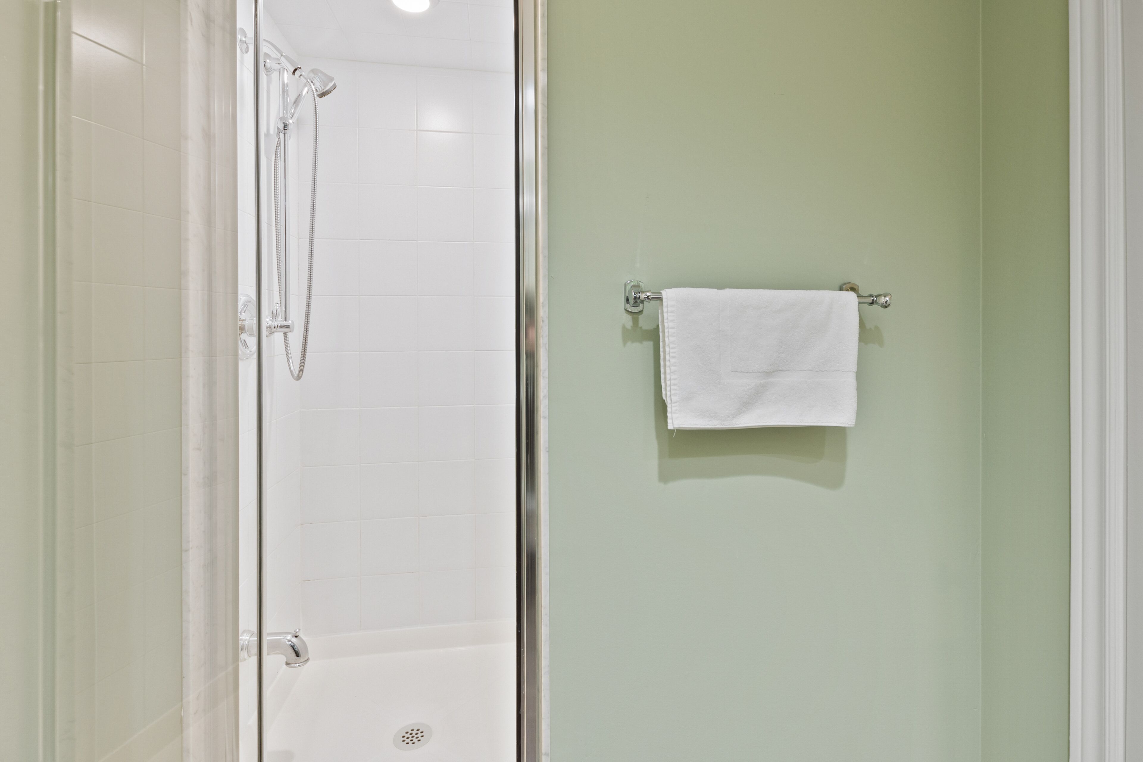 Ein Badezimmer mit Duschkabine aus Glas, einem weißen Handtuch an einem Halter und einer grünen Wand.