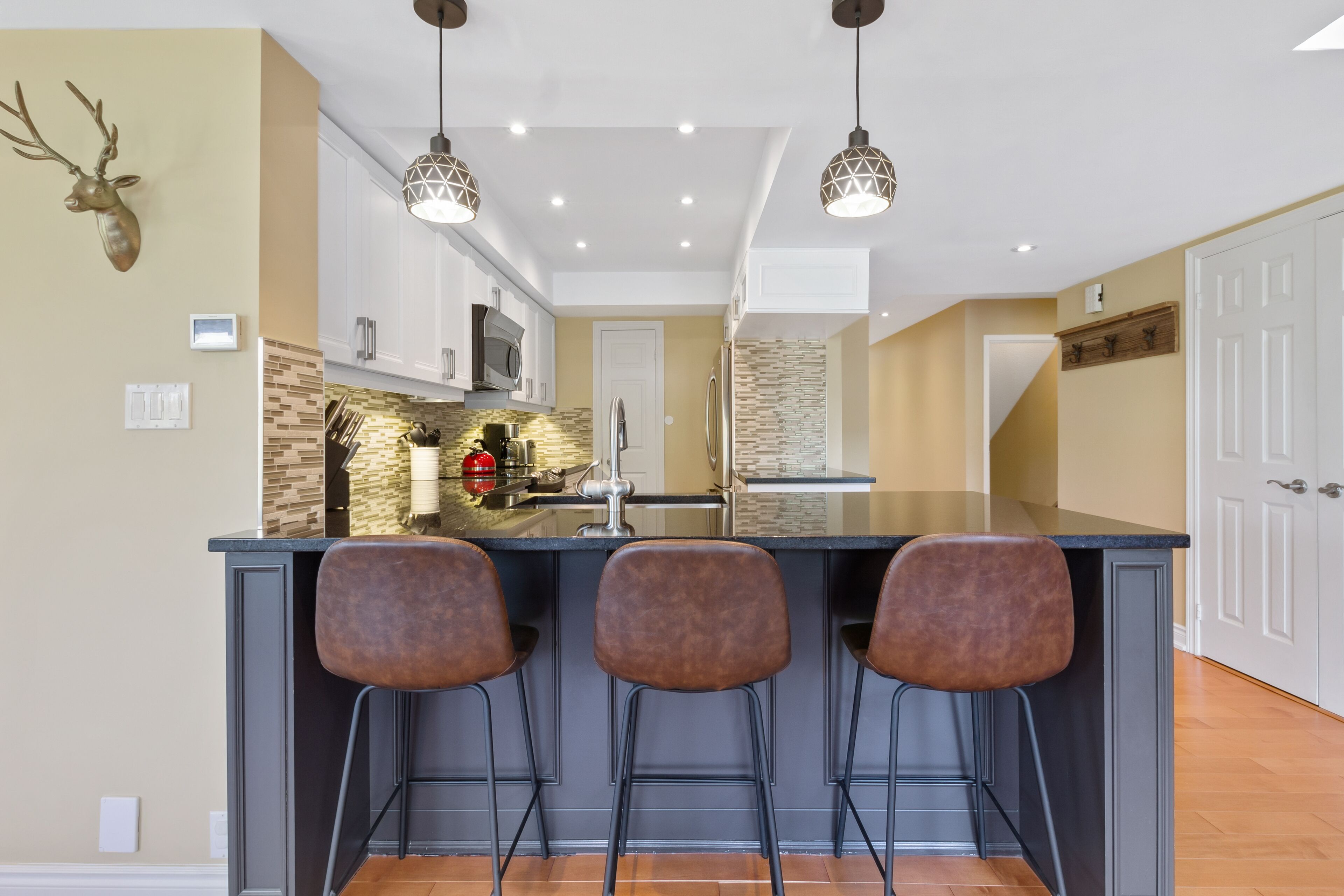 Una cocina con una isla central, taburetes de bar, iluminación colgante y una decoración de cabeza de venado.
