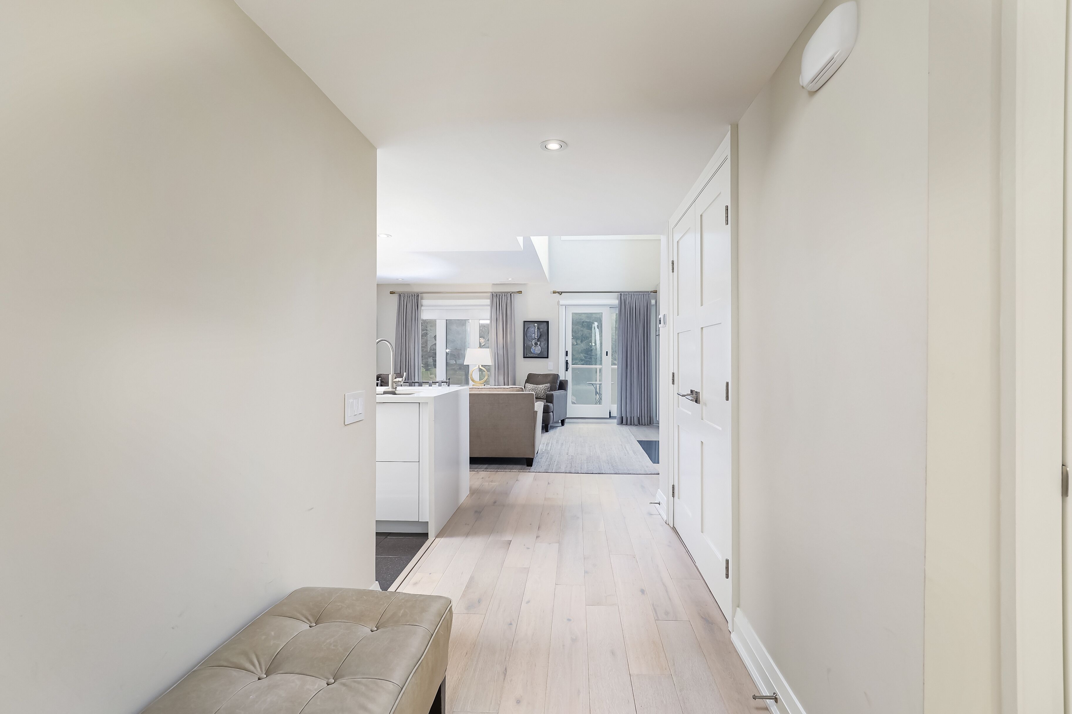 A narrow hallway with a bench, leading to a kitchen and a living area.