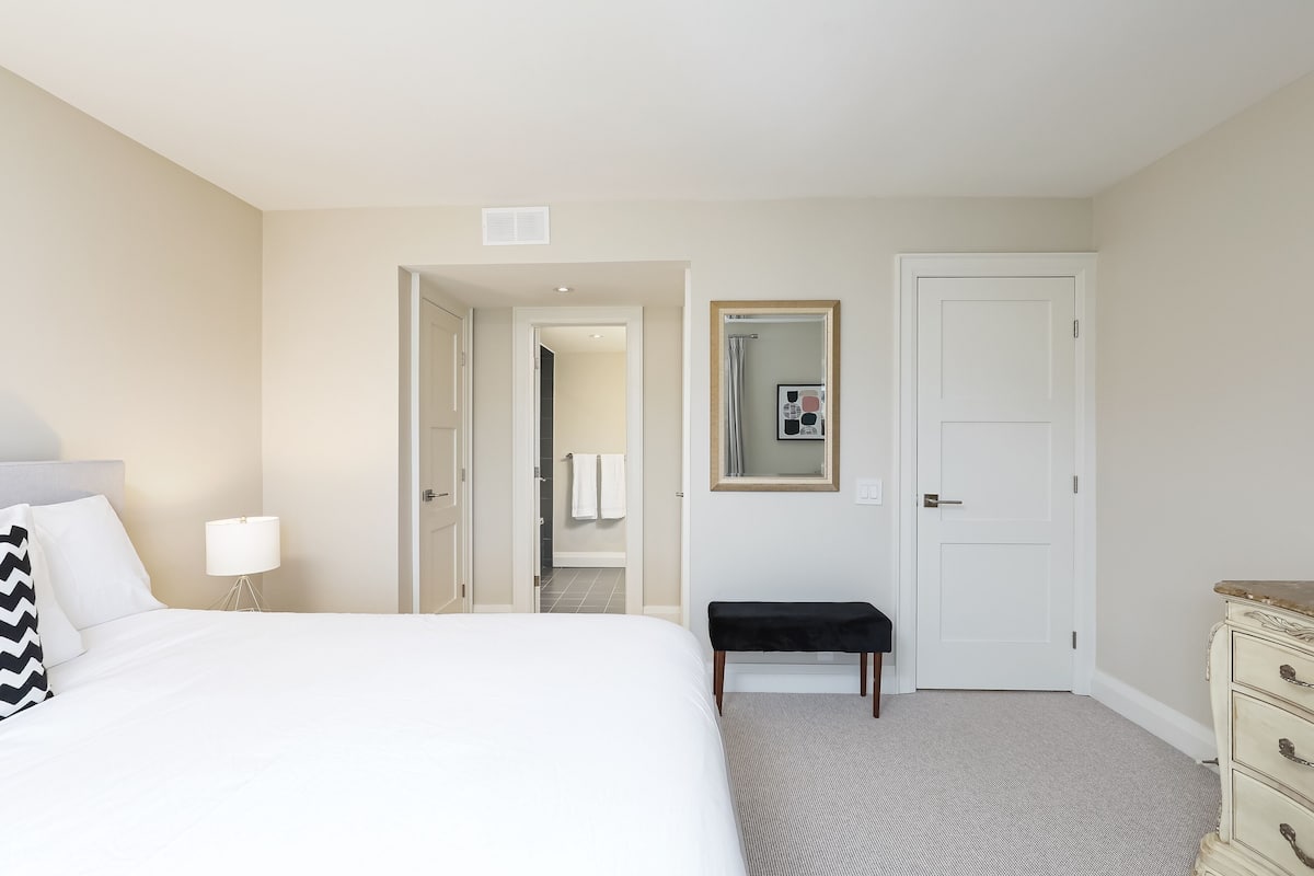 A hotel room with a bed, a bench, a dresser, a mirror, and a door leading to a bathroom.