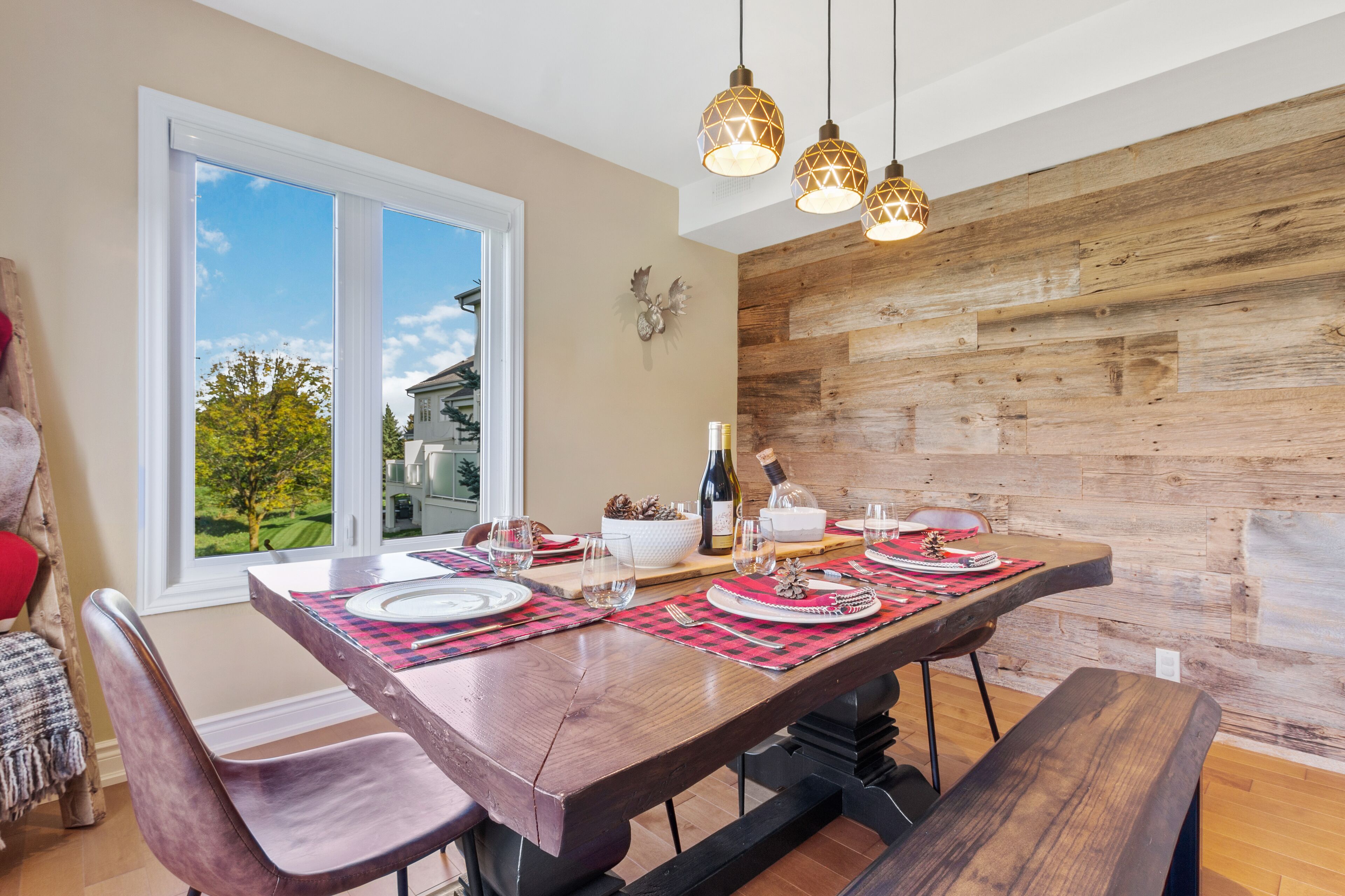 Un coin repas avec une table en bois dressée pour quatre personnes, une grande fenêtre et un mur en bois.
