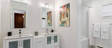 Une salle de bain moderne avec deux lavabos, un grand miroir et une douche.