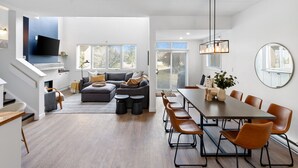 A modern living room with a gray sofa, a dining table with chairs, and a staircase leading to a loft area. - Wintergreen Condos (The Blue Mountains)