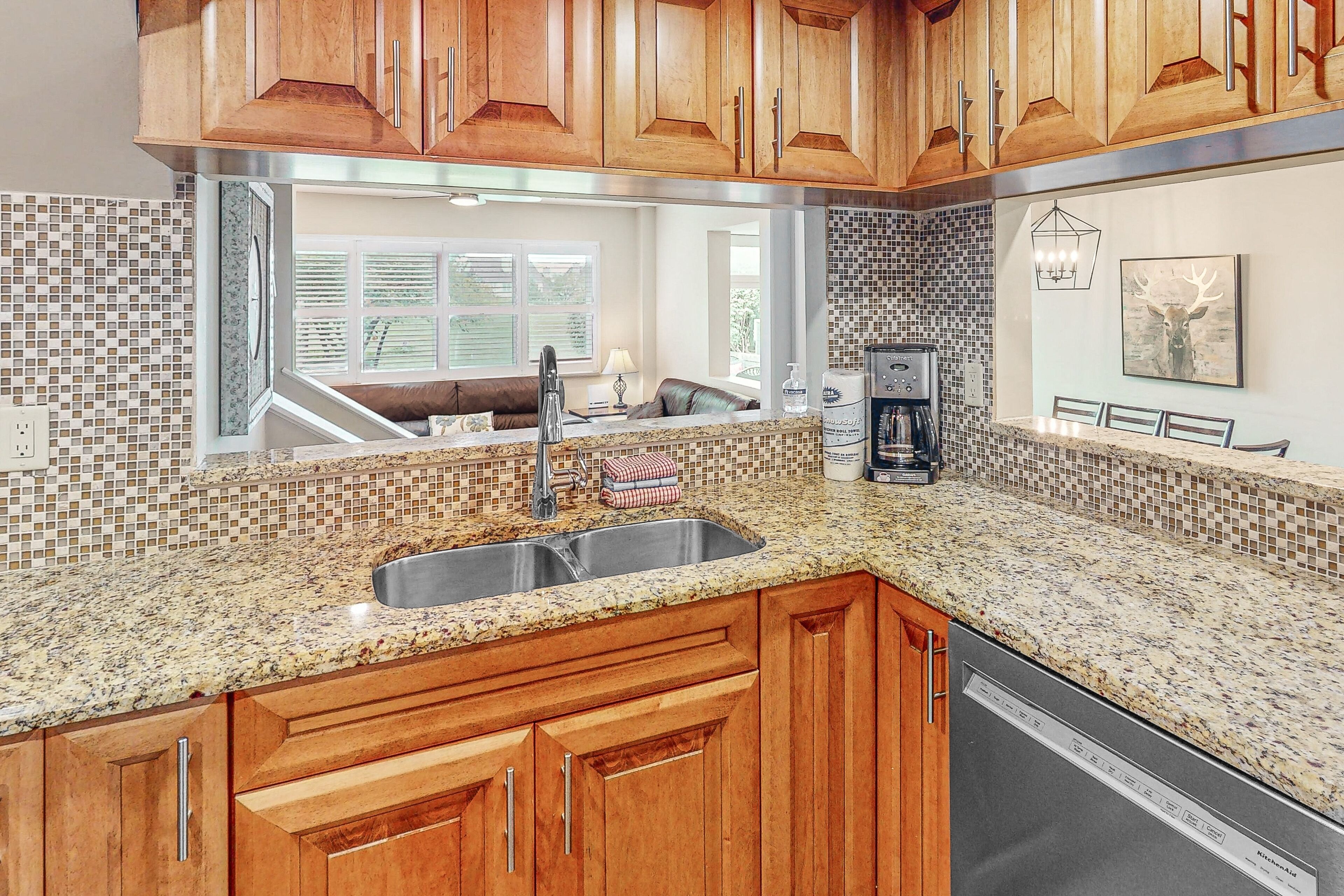 A kitchen with wooden cabinets, a granite countertop, a built-in dishwasher, and a window with blinds.