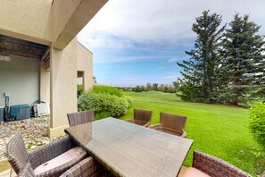 An outdoor patio with wicker furniture and a view of a green lawn and trees.