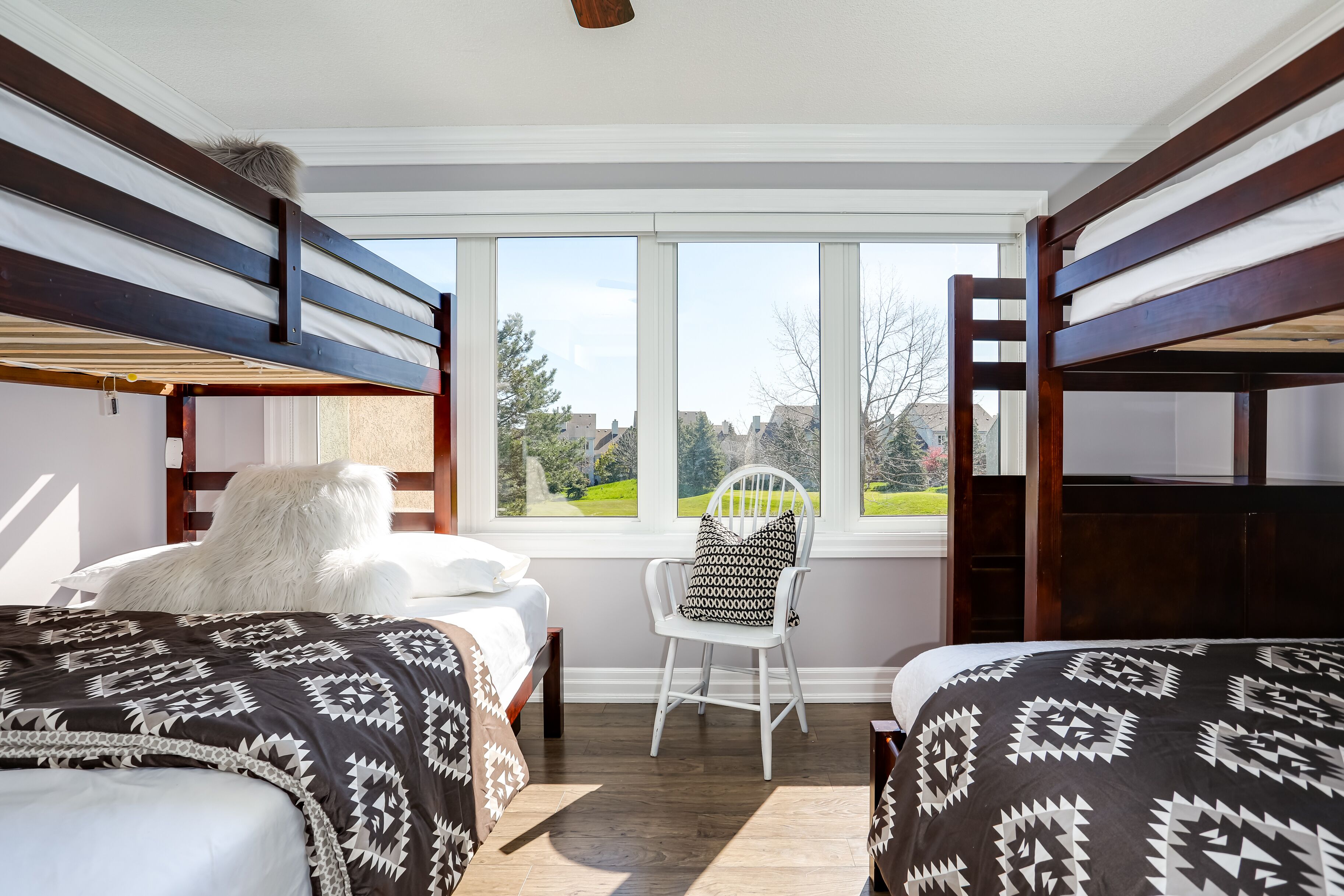 A room with bunk beds, a white chair, and a large window with a view of a green landscape.