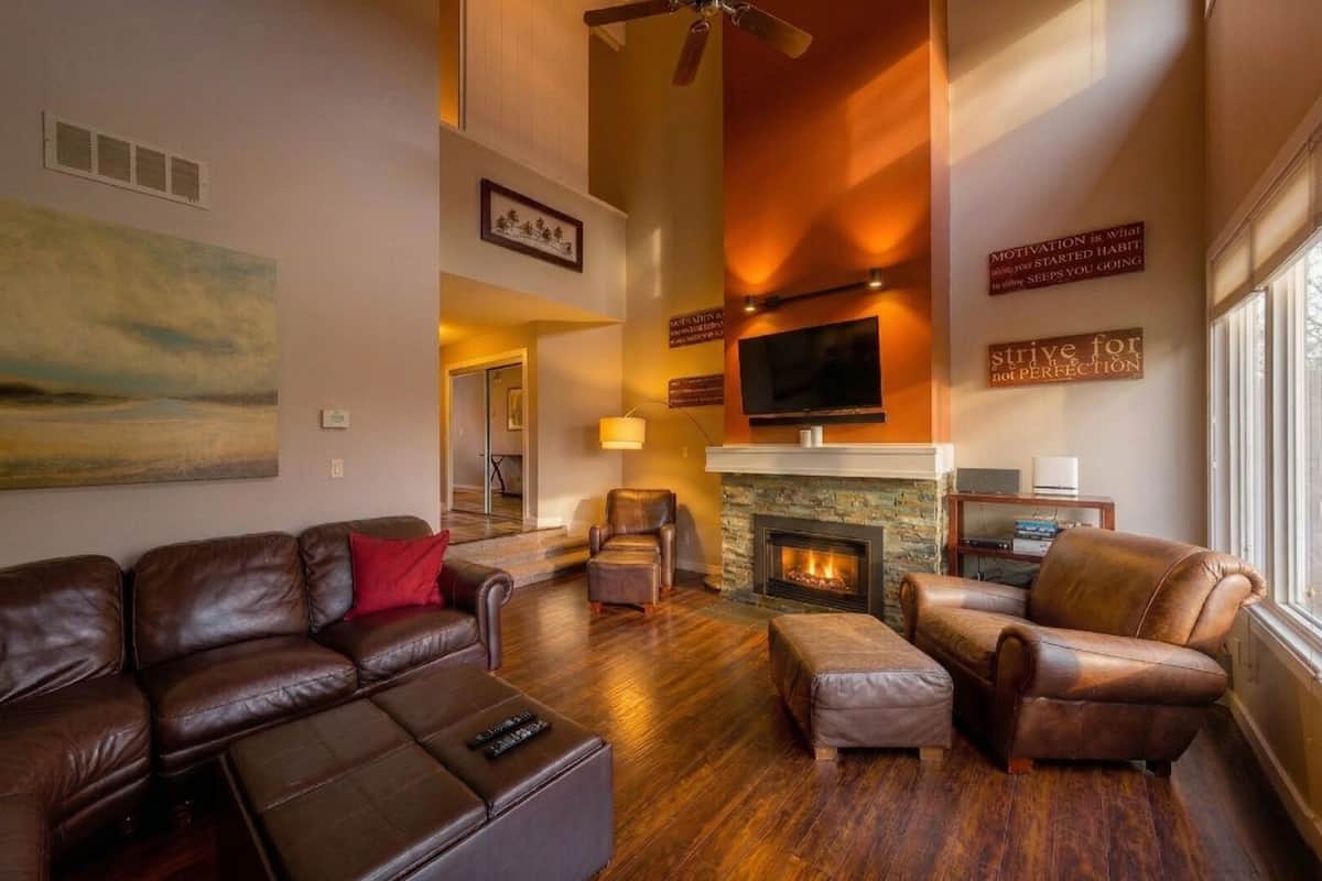 A spacious living room with leather sofas, a fireplace, a television, and motivational wall art.