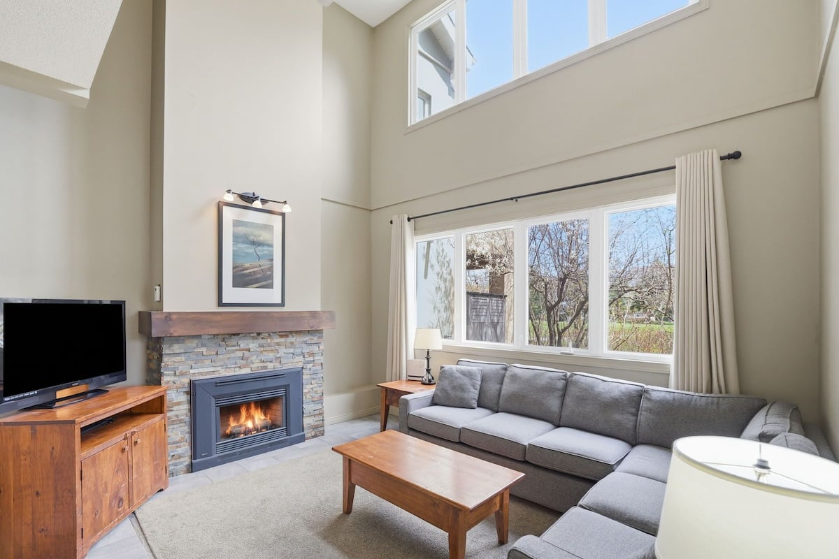 A living room with a fireplace, a sofa, a coffee table, a TV, and a window with curtains.