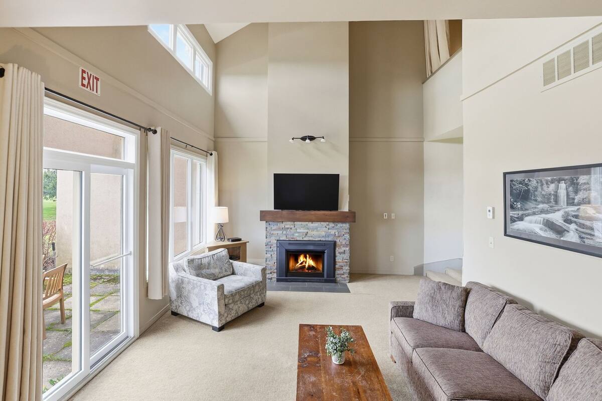A living room with a fireplace, a sofa, a coffee table, and a large window.