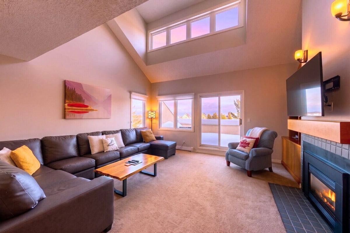 A living room with a sofa set, a coffee table, a fireplace, and a large window with a view.