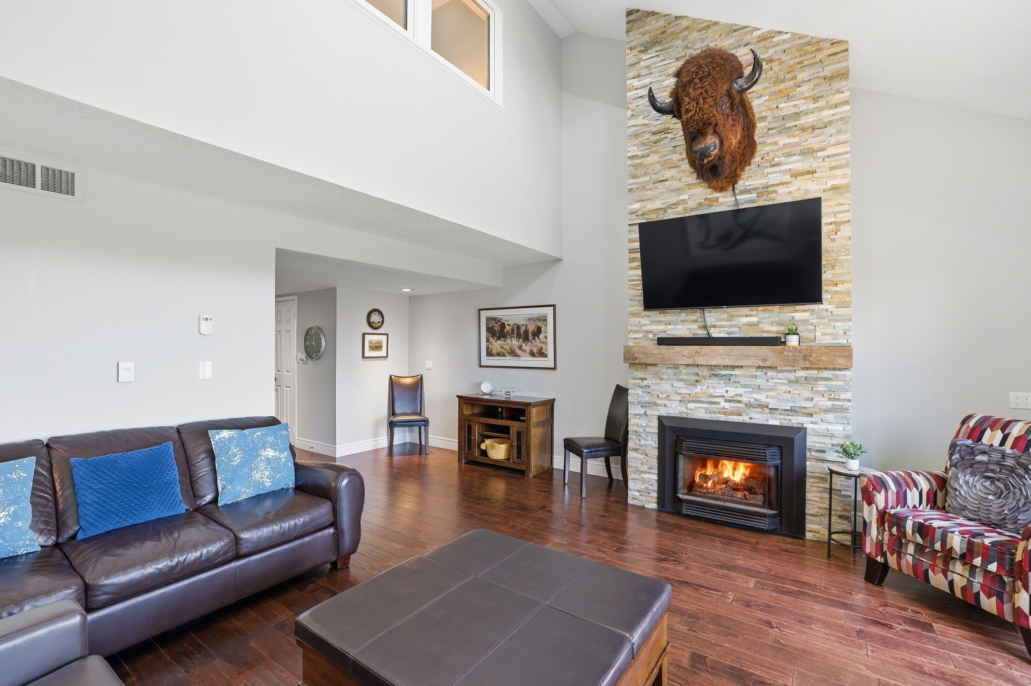 A spacious living room with a stone fireplace, a mounted TV, and a large bull head decoration on the wall.