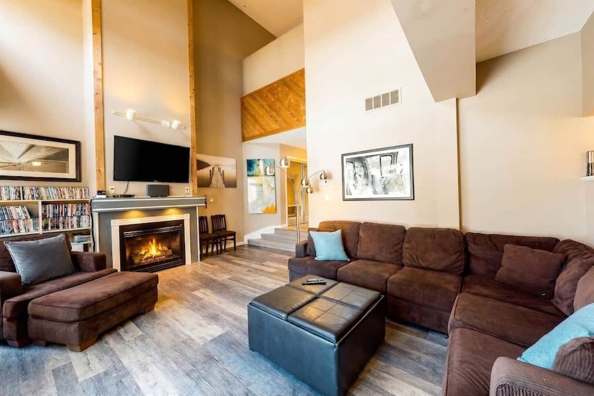 A spacious living room with a fireplace, a large sofa, a coffee table, and a bookshelf filled with books.