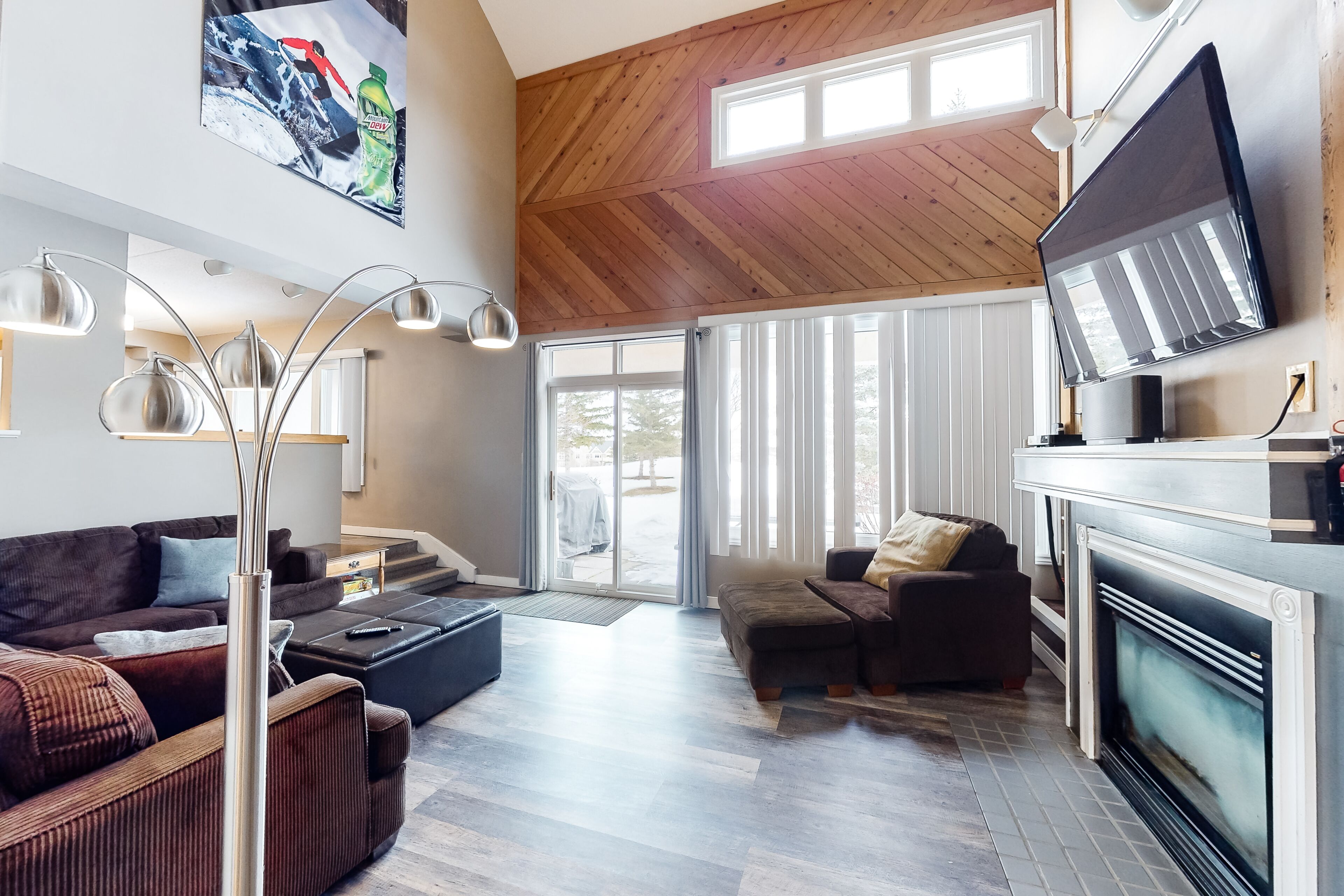 En rummelig stue med pejs, store vinduer og et hvælvet loft med træbjælker.