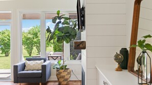 A modern living room with a grey armchair, a large potted plant, and a wooden floor. - Wintergreen Condos (The Blue Mountains)