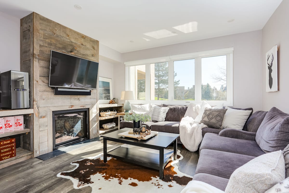 A modern living room with a fireplace, a large flat-screen TV, a gray sofa, and a cowhide rug.