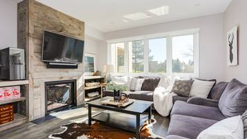 A modern living room with a fireplace, a large flat-screen TV, a gray sofa, and a cowhide rug.