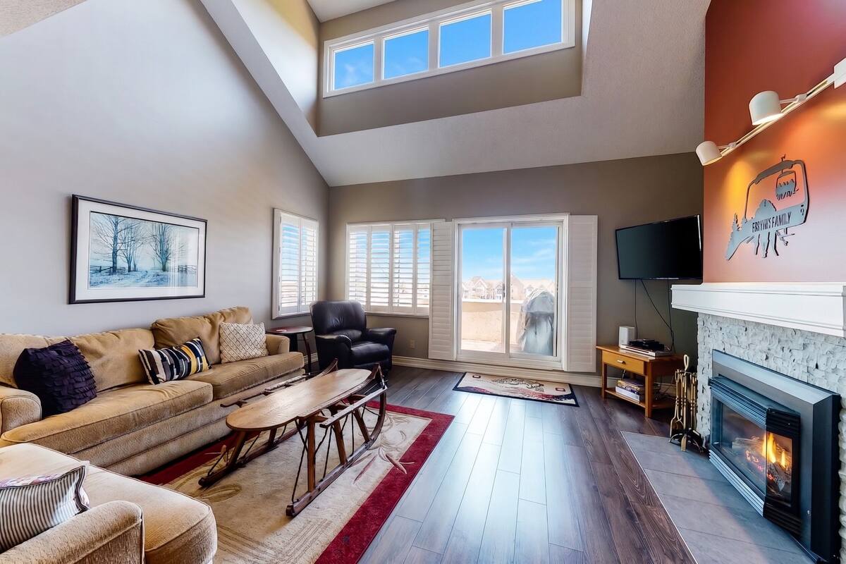 A spacious living room with a fireplace, a sofa set, a dining table, and a large window.
