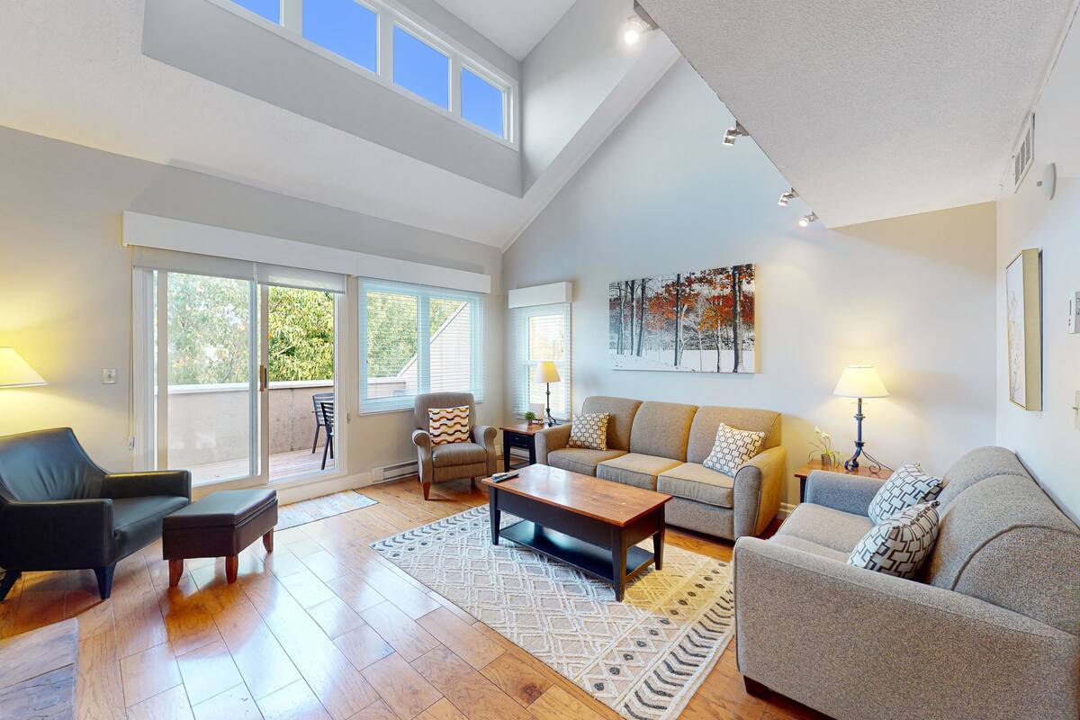 A spacious living room with a high ceiling, large windows, and a modern fireplace.
