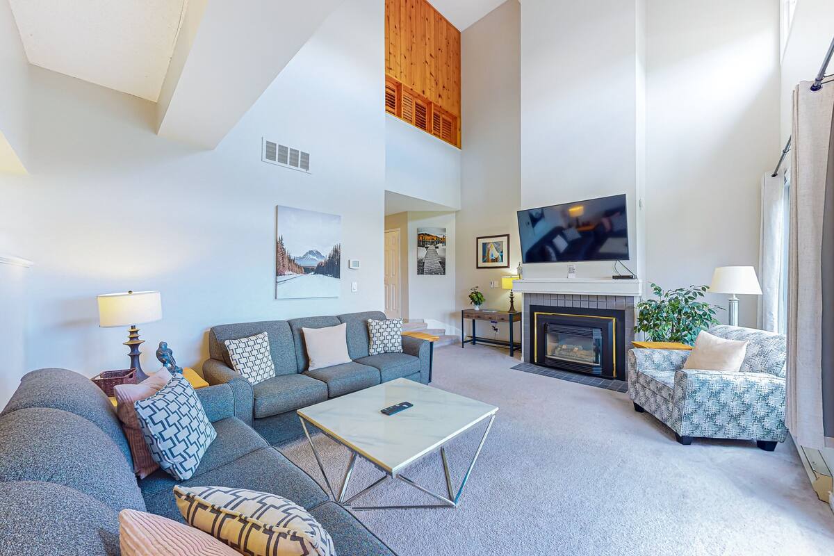 A spacious living room with a high ceiling, a fireplace, a television, and a comfortable seating area.