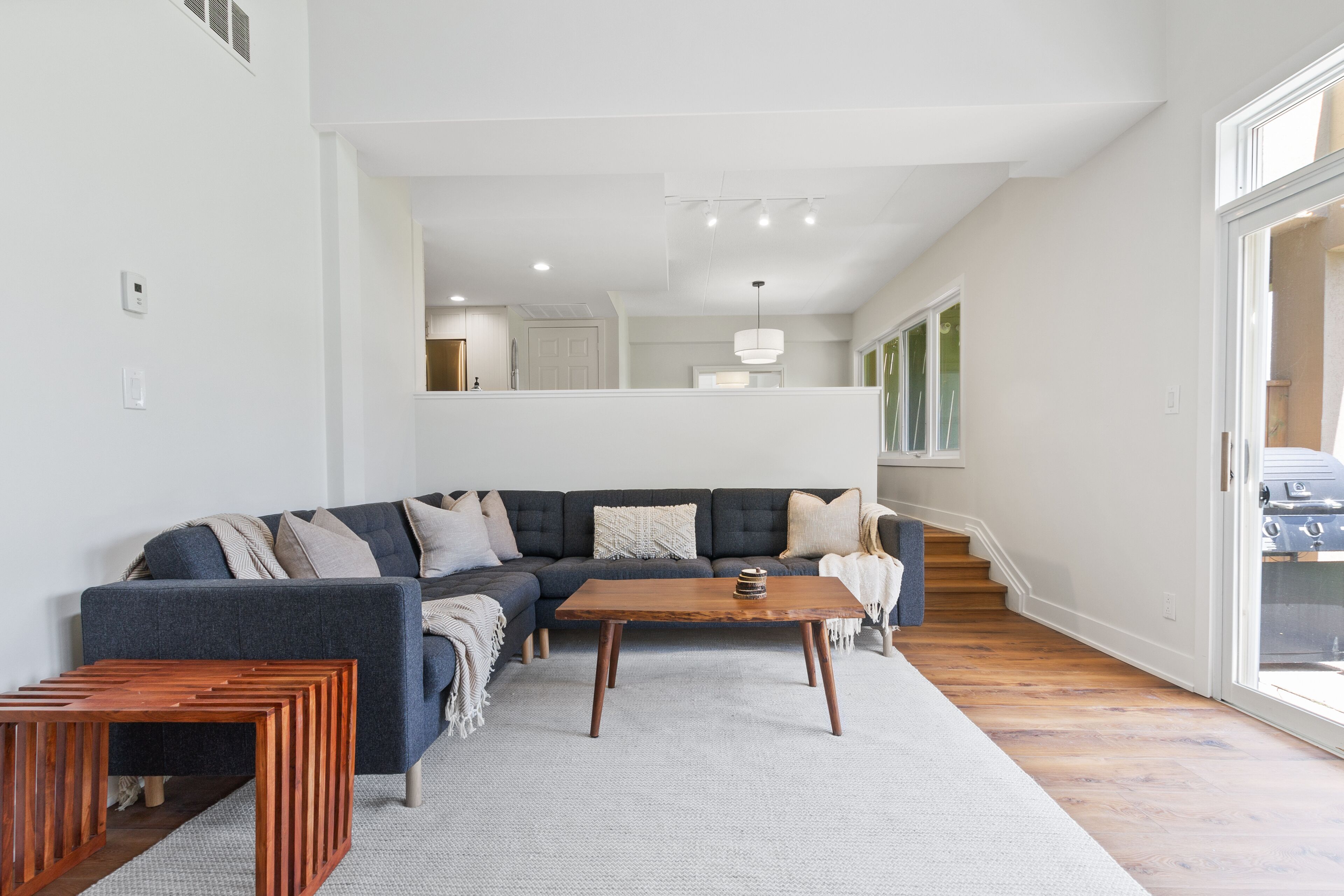 Ein modernes Wohnzimmer mit einem dunkelblauen Ecksofa, einem Holztisch und einem hellgrauen Teppich.