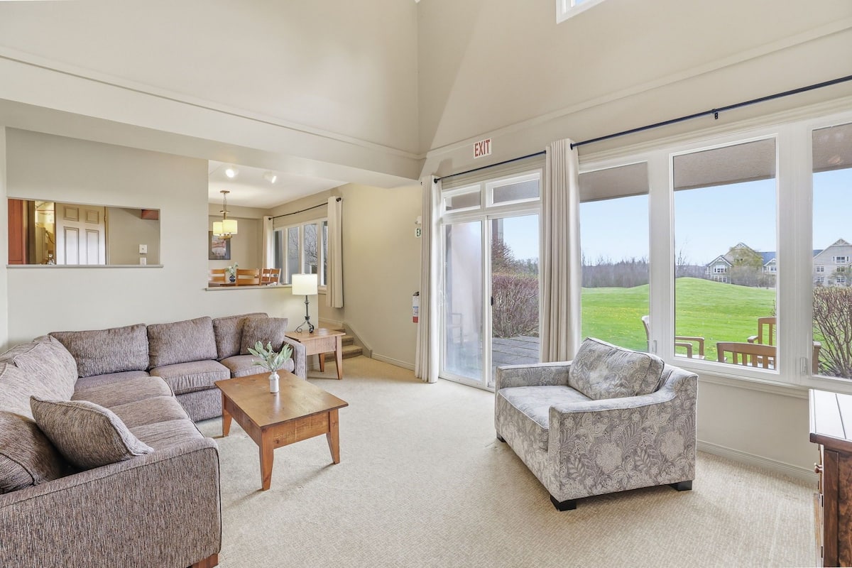 A spacious living room with a large sectional sofa, a patterned armchair, and a wooden coffee table.
