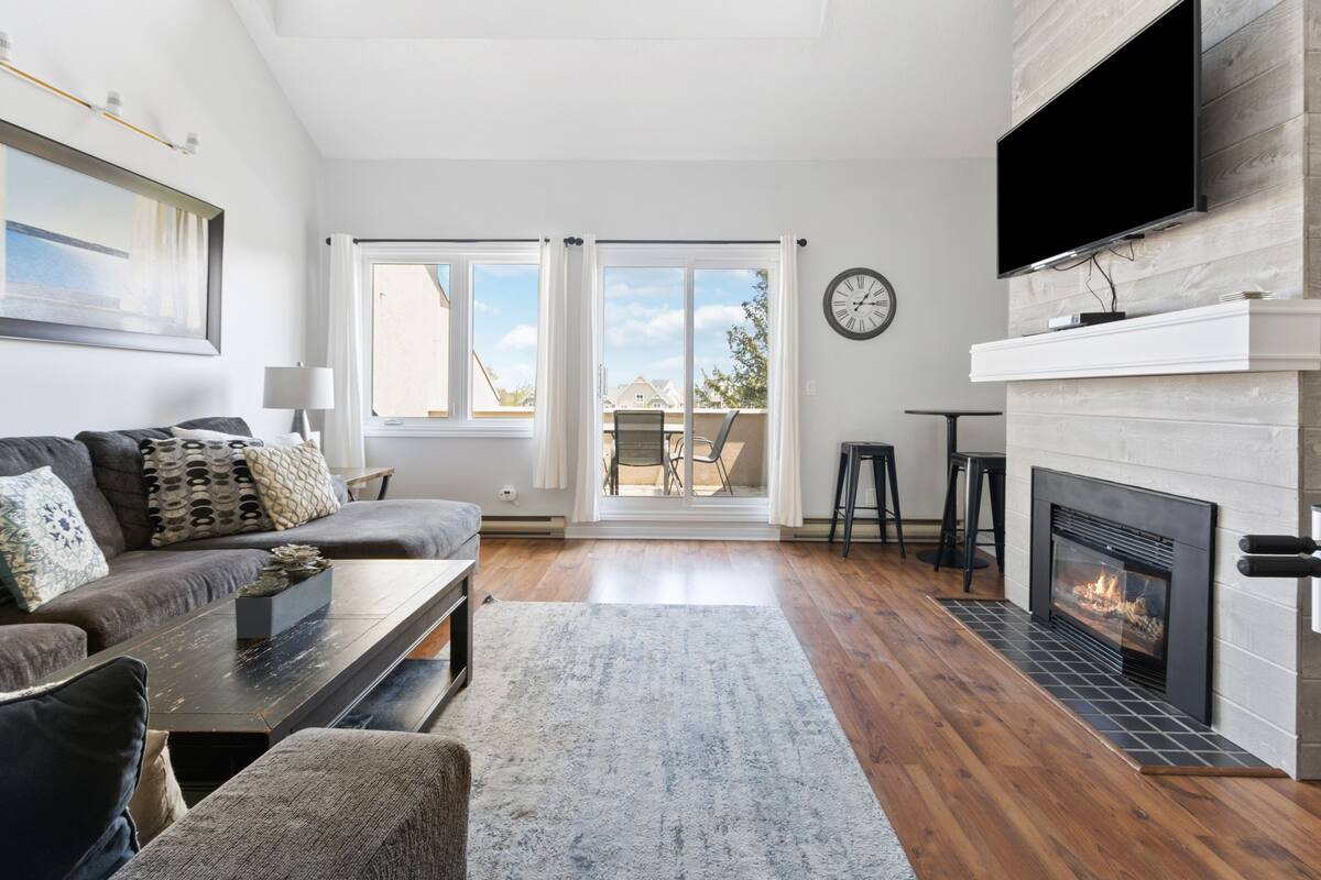 A modern living room with a fireplace, a sofa, a coffee table, and a television mounted on the wall.