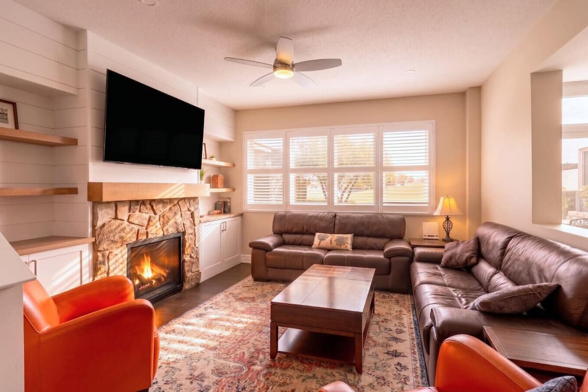 A living room with a fireplace, leather sofas, a coffee table, and a TV mounted on the wall.
