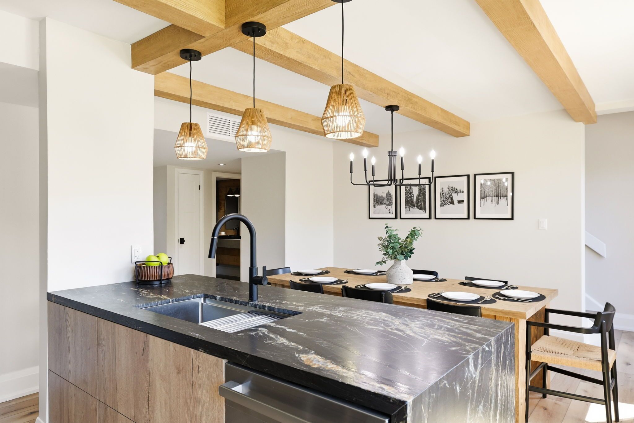 A modern kitchen with a large island, pendant lights, and a dining area with a table set for four.