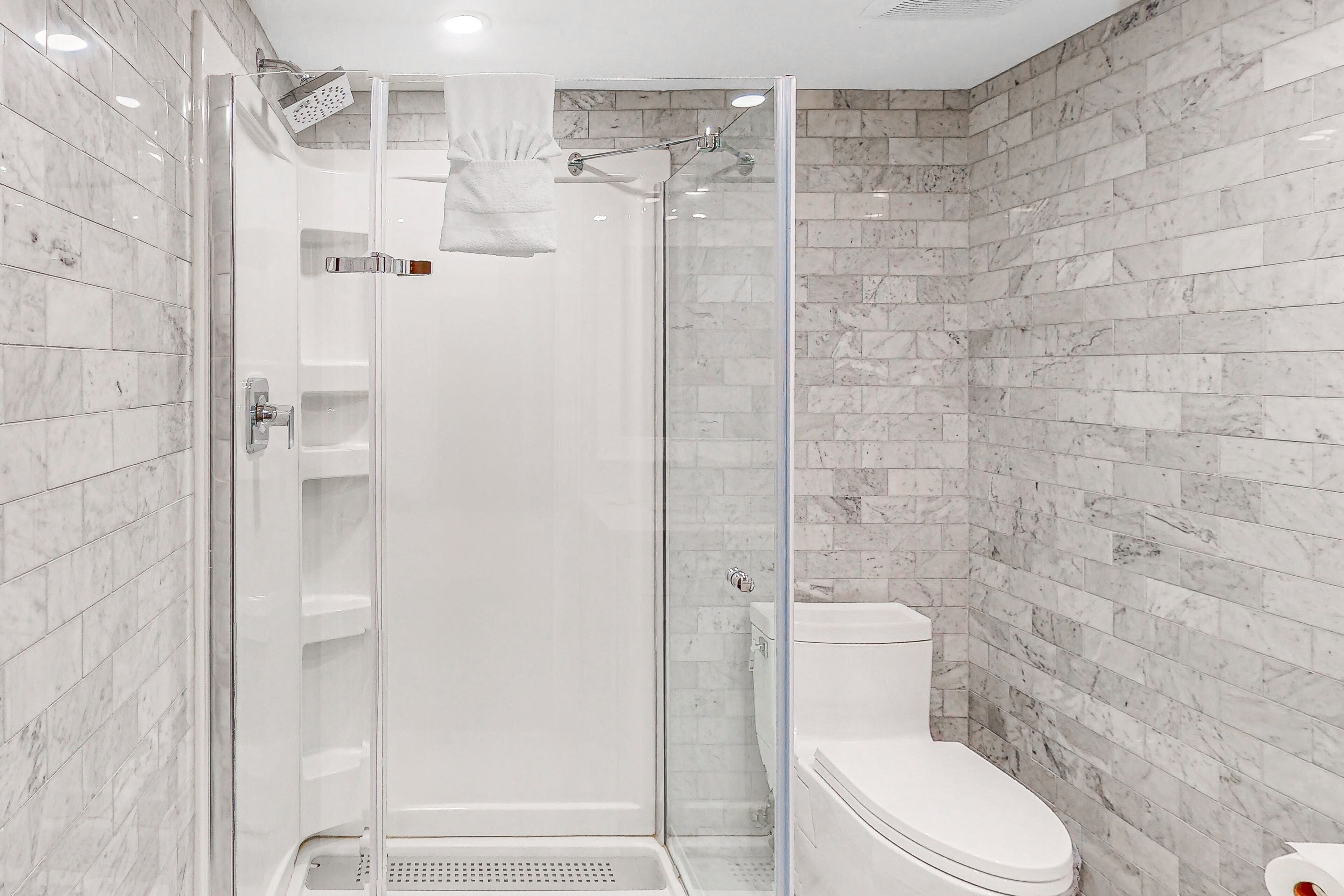 A modern bathroom with a glass-enclosed shower, a white toilet, and marble tiles.