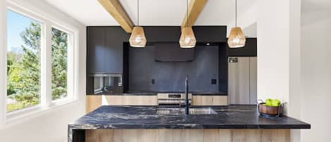 Una cocina moderna con una isla central, encimeras negras, taburetes de madera e iluminación colgante.