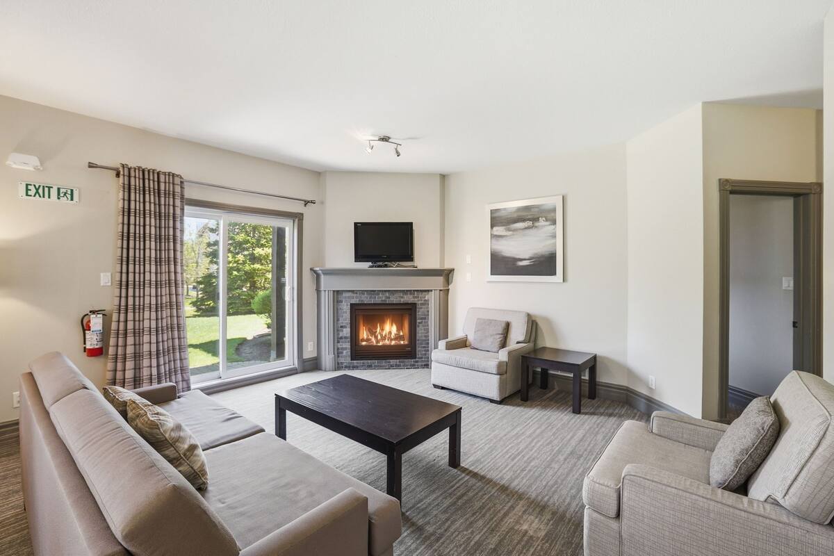 Ein Wohnzimmer mit Kamin, Sofas, einem Fernseher und Blick durch die Glastür.