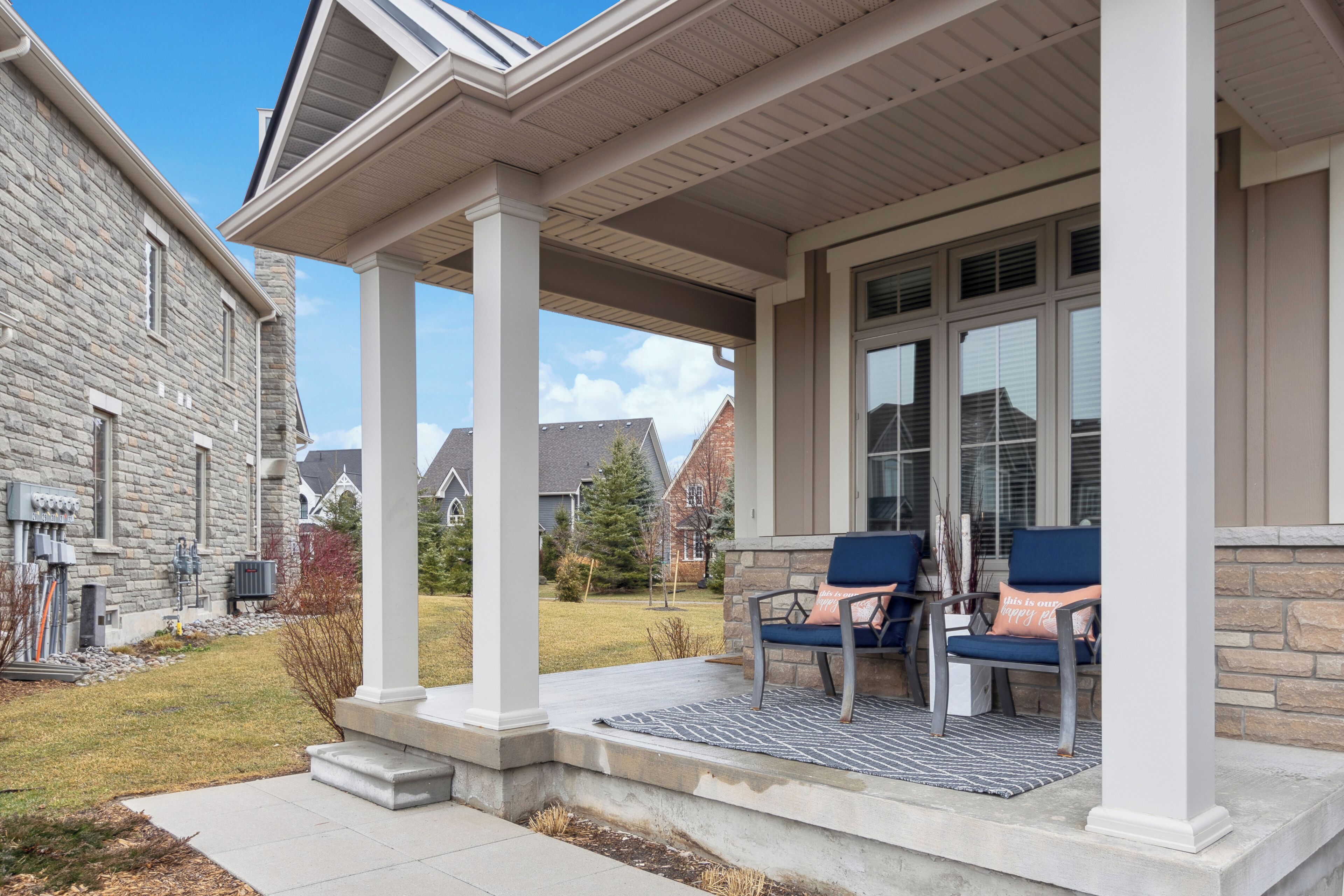 A covered porch with two blue chairs and a patterned rug.