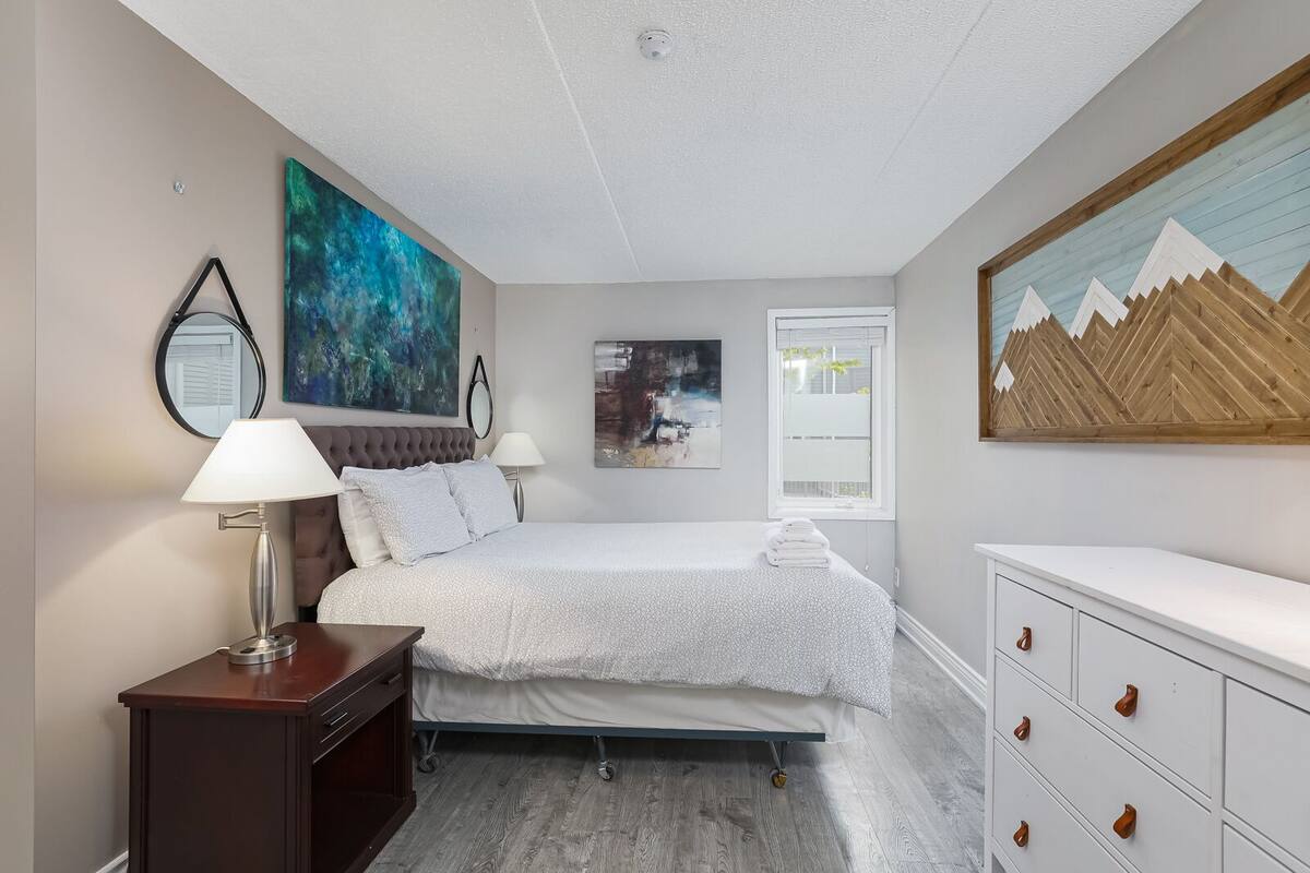 A bedroom with a bed, bedside tables, a dresser, and artwork on the walls.