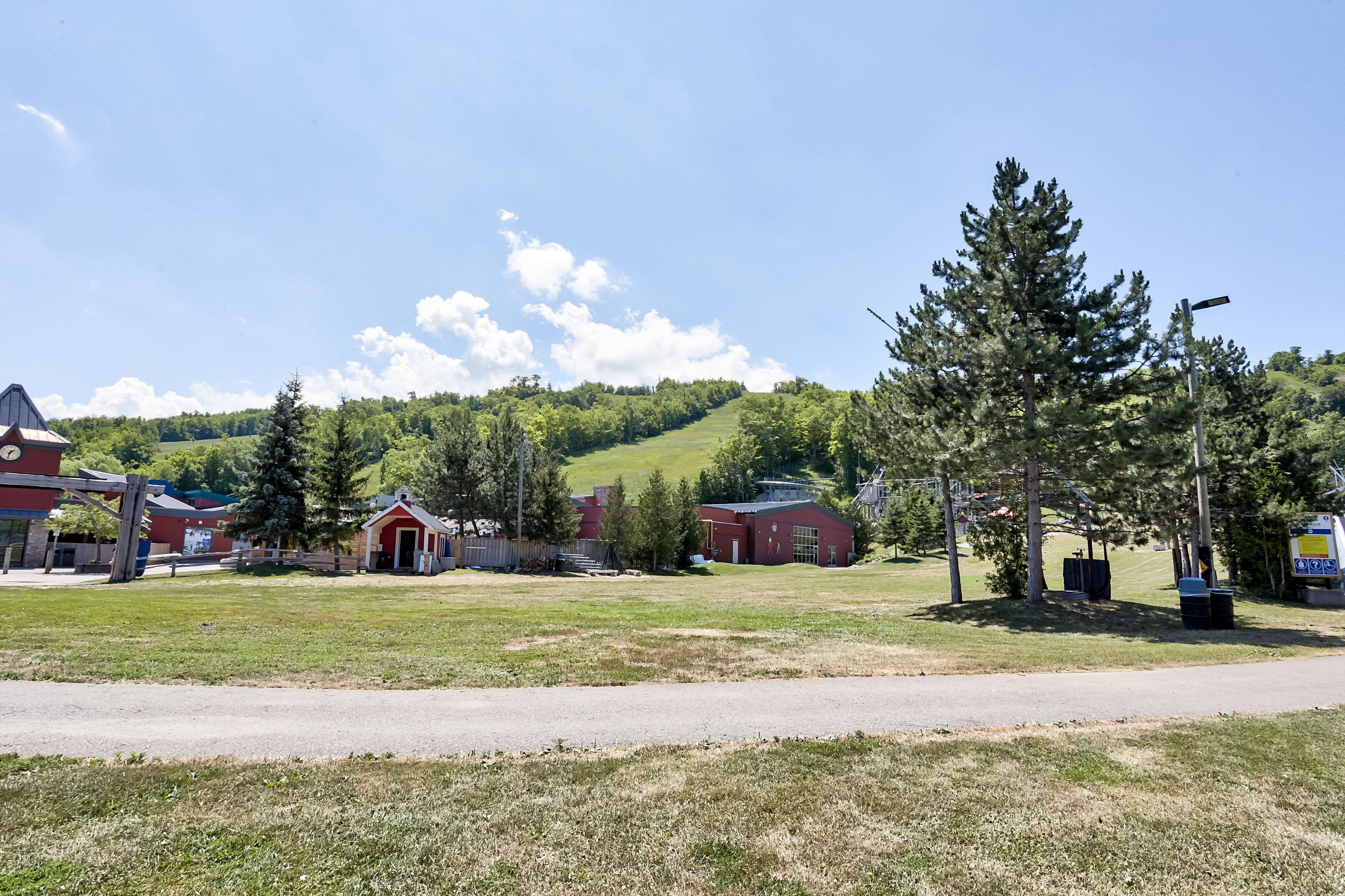 A rural landscape with a small building, a road, and a hill in the background.