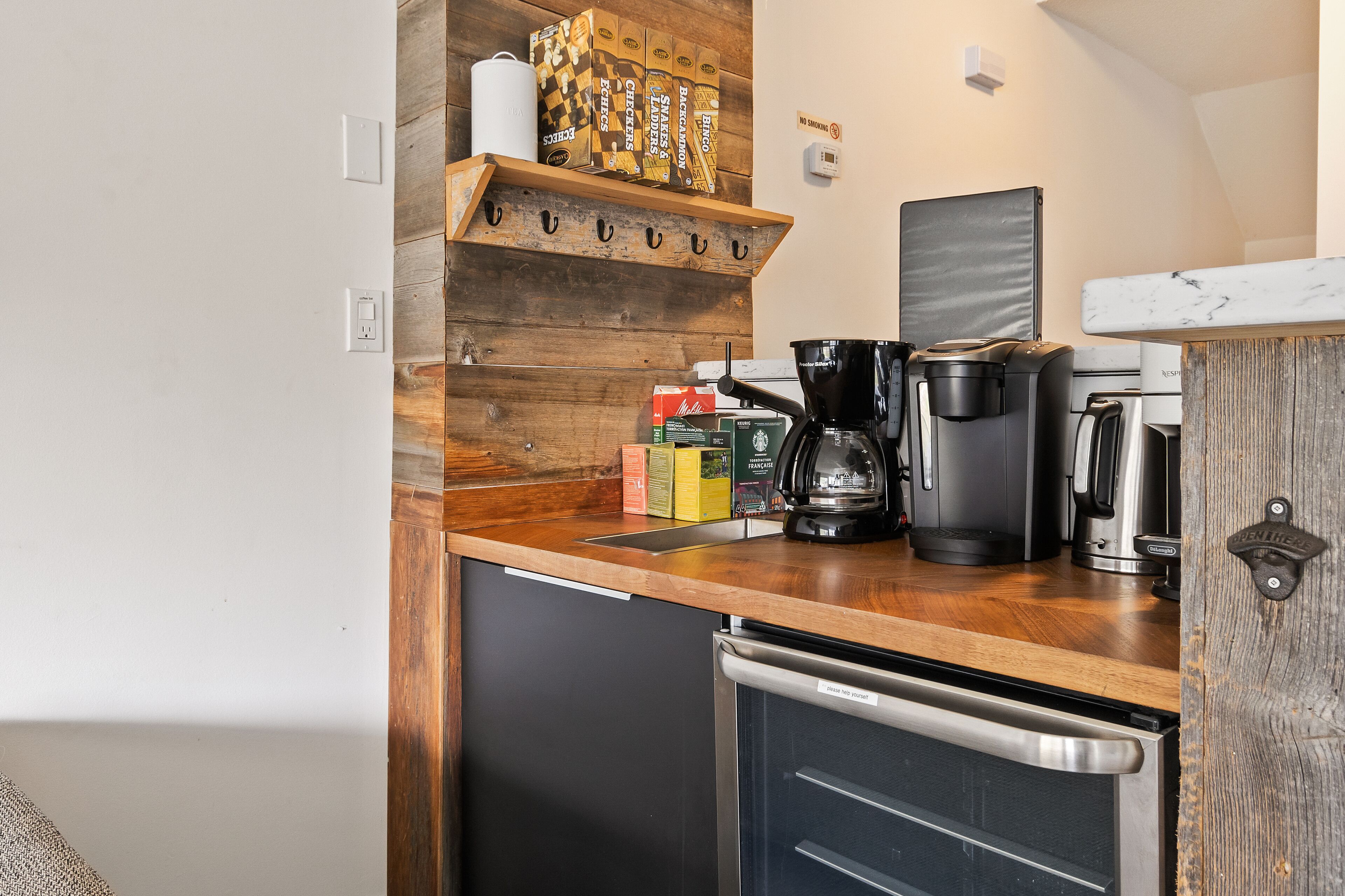 A compact kitchen with a wooden shelf holding coffee boxes, a coffee maker, and a kettle.