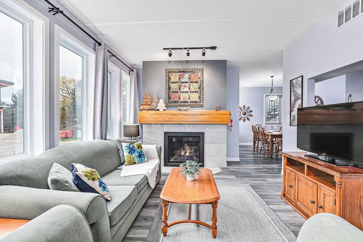 A spacious living room with a grey sofa, a wooden coffee table, a fireplace, and a TV.