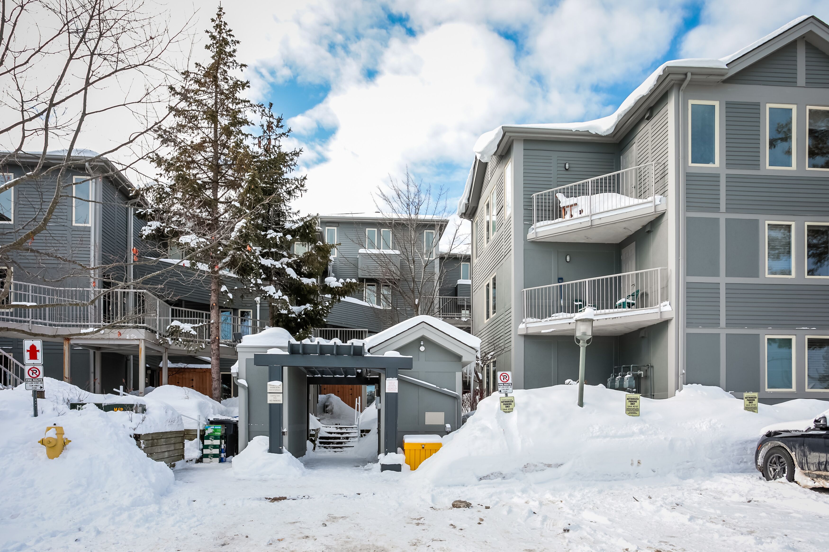 Un edificio residencial con varios balcones, una entrada protegida por un portón y un camino de acceso cubierto de nieve.