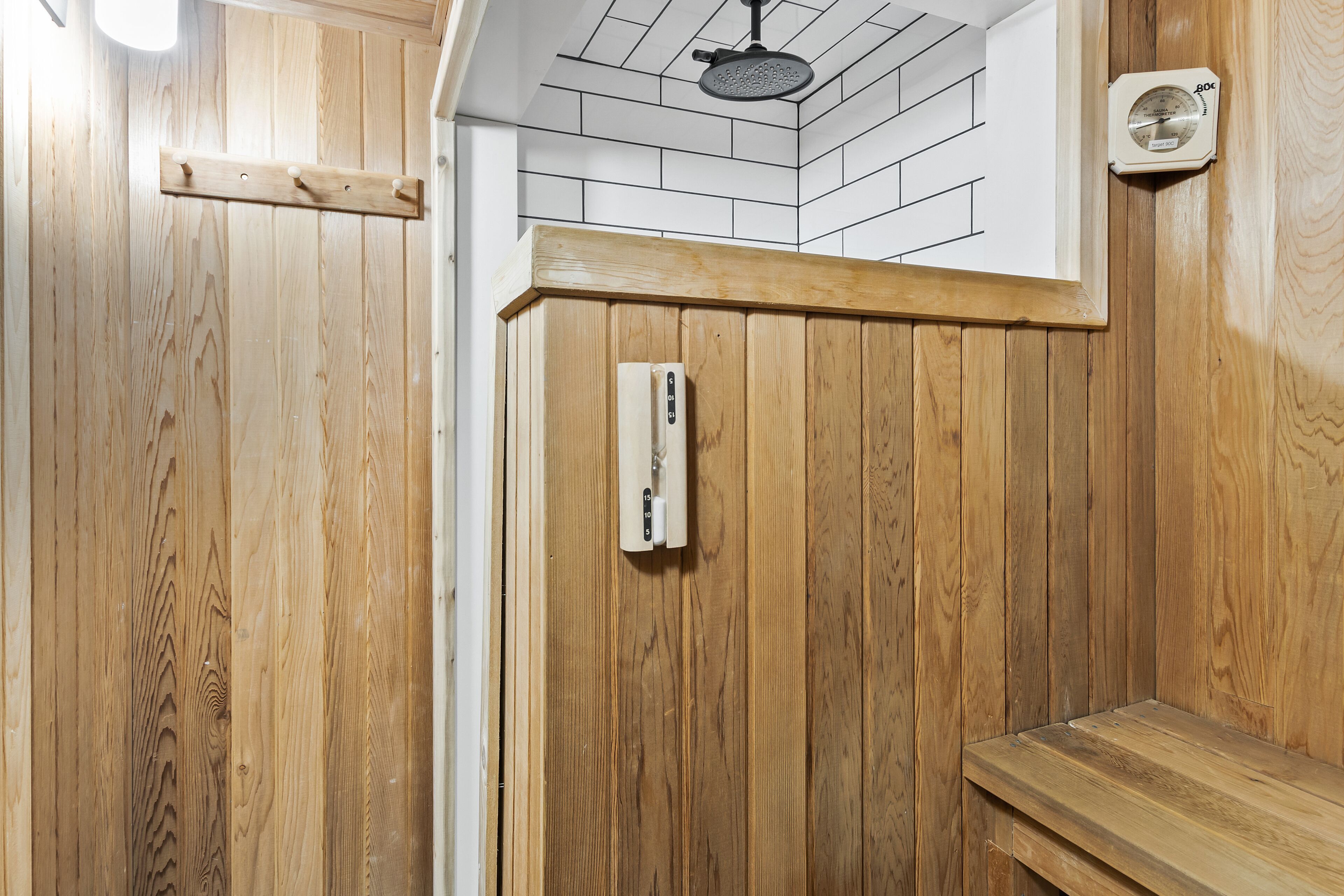 A wooden sauna with a bench, a ceiling-mounted showerhead, and a wall-mounted thermometer.