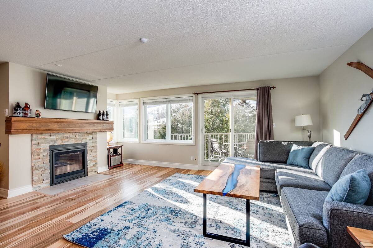 A living room with a fireplace, a sofa, a coffee table, and a view of the outdoors.