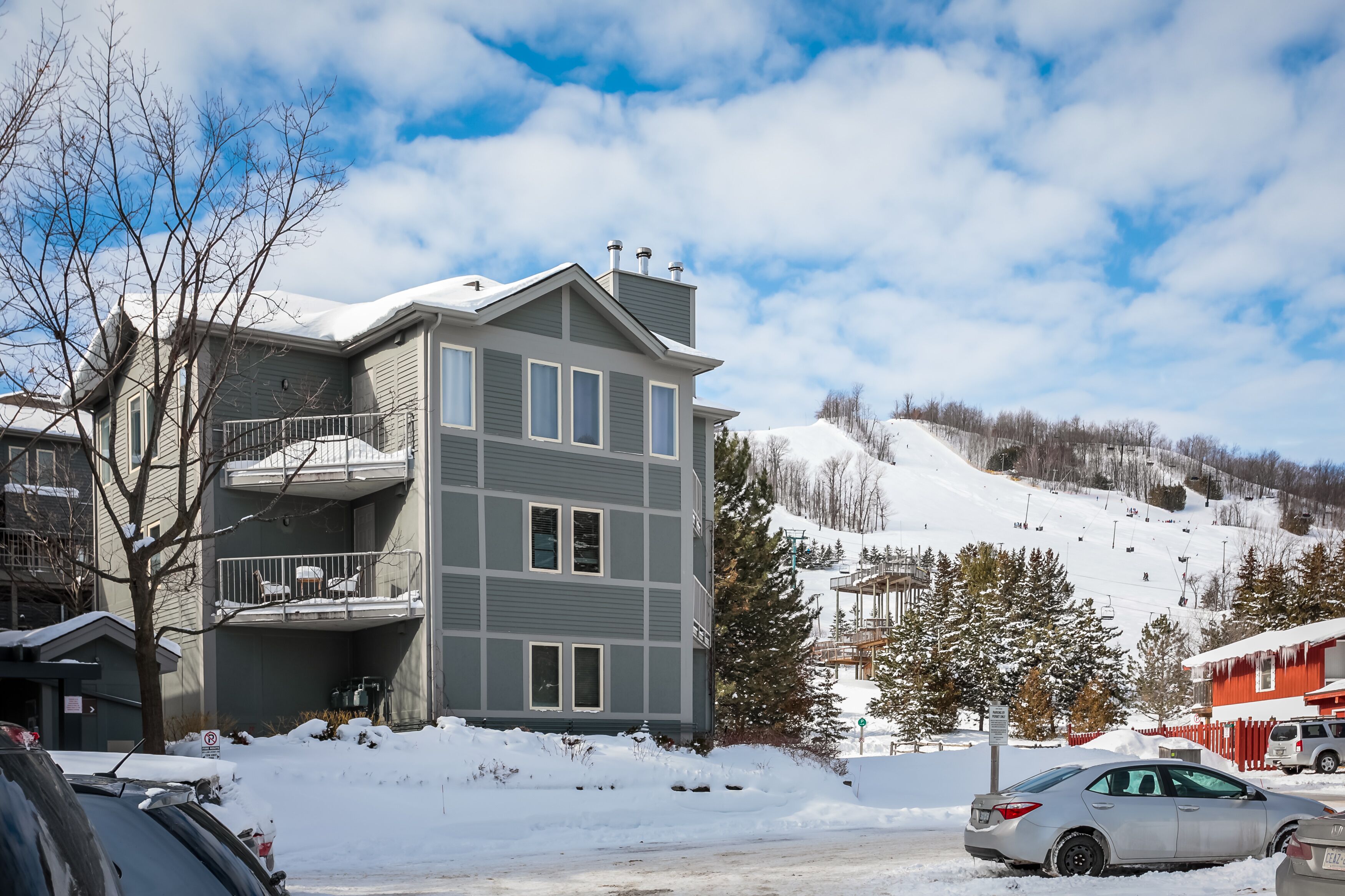 A multi-story building with a balcony, a ski slope in the background, and a snow-covered ground.