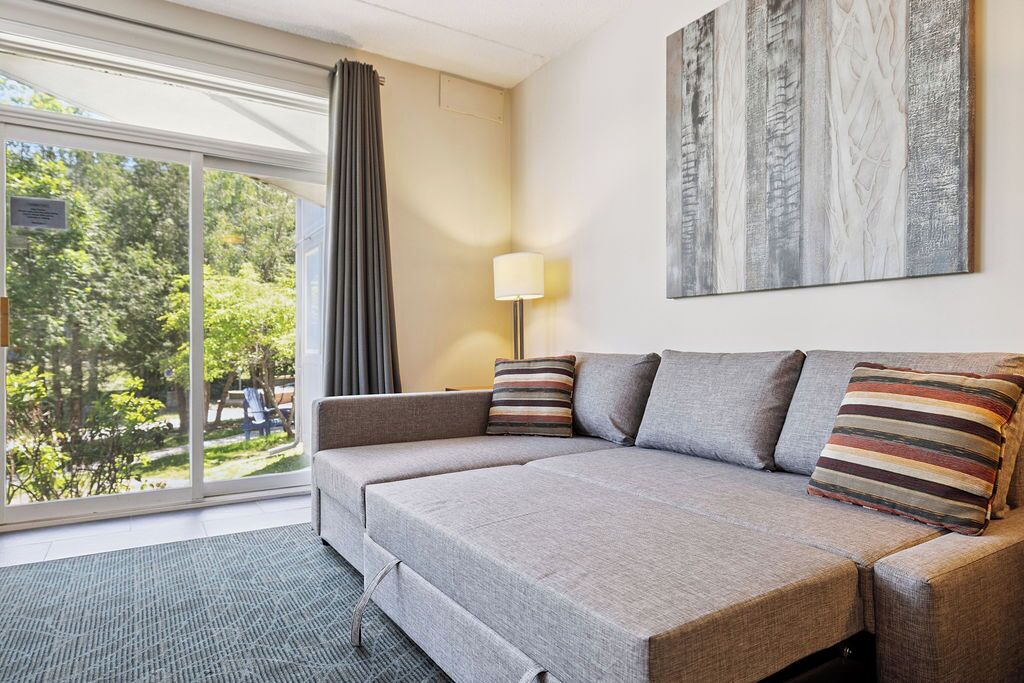 A modern hotel room with a grey sofa, a lamp, and a large window with curtains.
