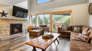 A spacious living room with a stone fireplace, large windows, and a comfortable seating area. - Cachet Crossing Chalets (The Blue Mountains)