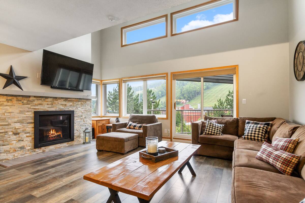 A spacious living room with a stone fireplace, large windows, and a comfortable seating area.