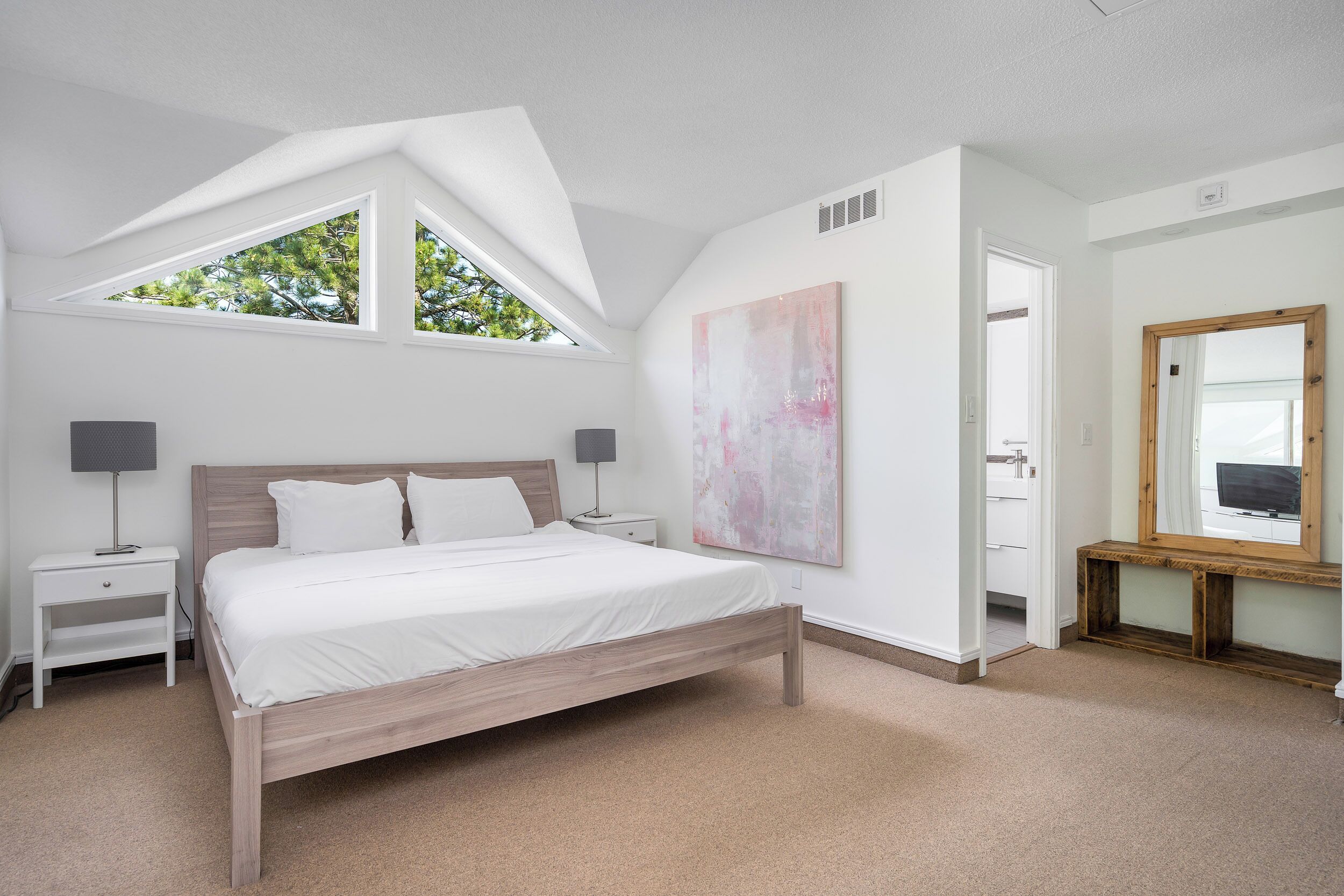Um quarto com claraboia, uma cama grande, mesas de cabeceira, um espelho e um quadro na parede.