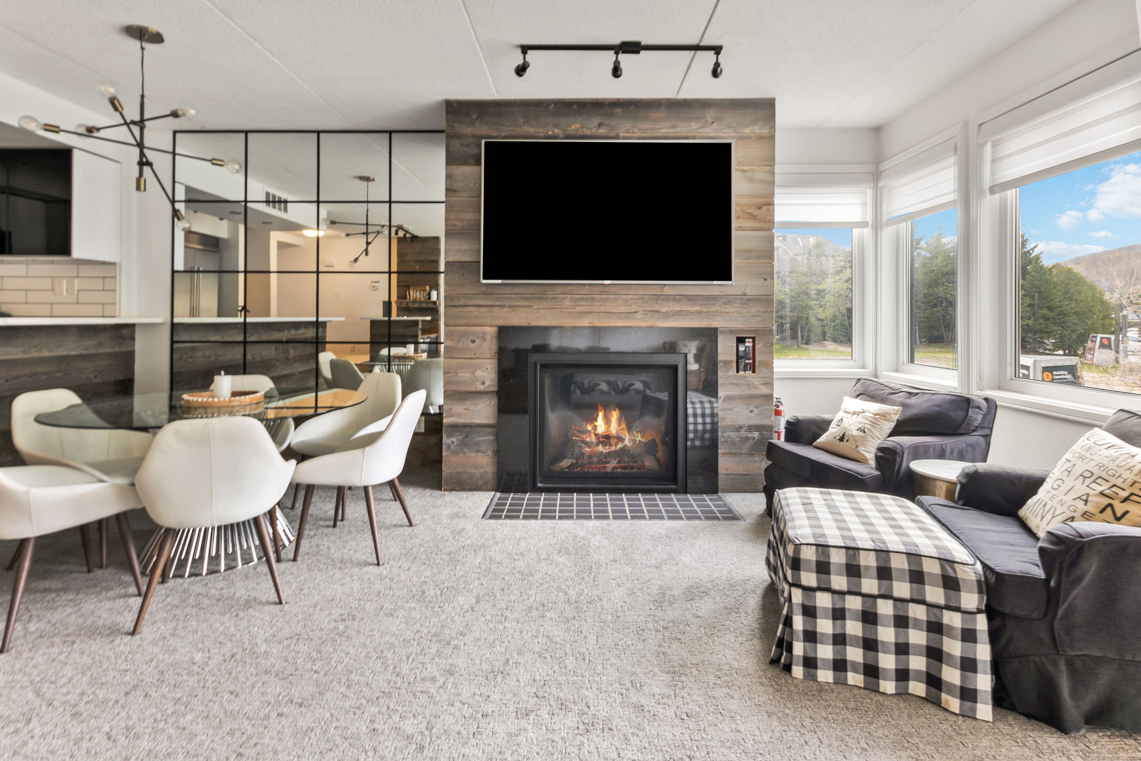 A modern living room with a fireplace, a dining area with a glass table, and a sofa with a checkered ottoman.